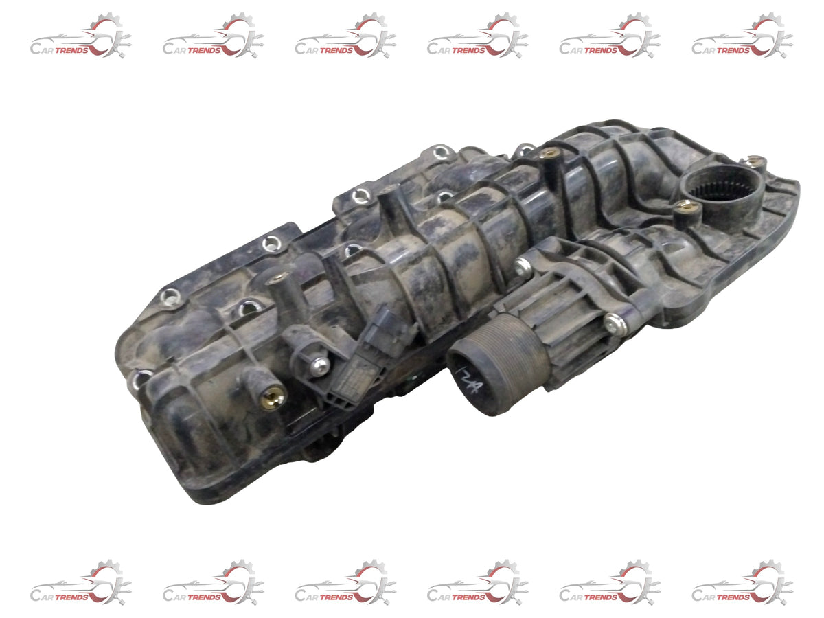 General Motors Chevrolet Enjoy manifold intake, close-up view showing the black plastic engine part with hoses and fittings.
