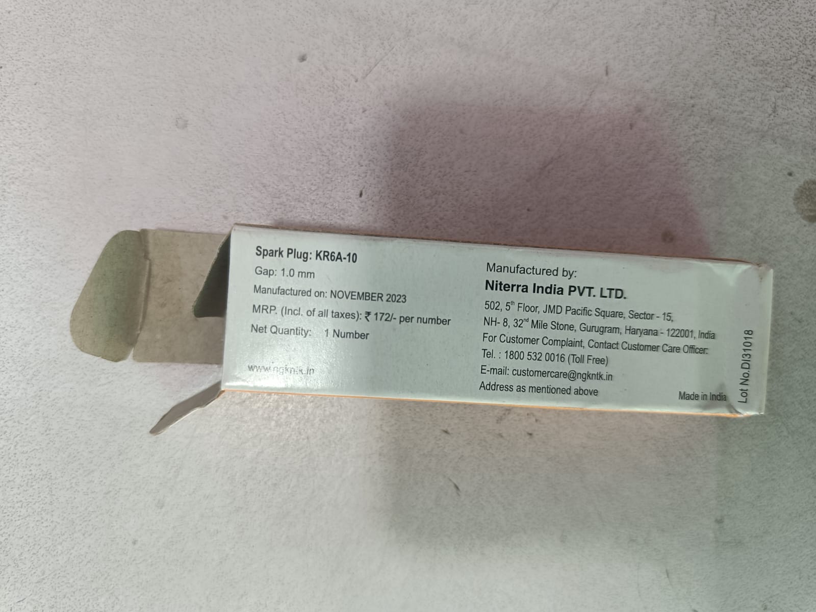 NGK Spark Plug WagonR K Series KR6A10 installed in a vehicle, showing the spark plug with visible metal electrode and ceramic insulator