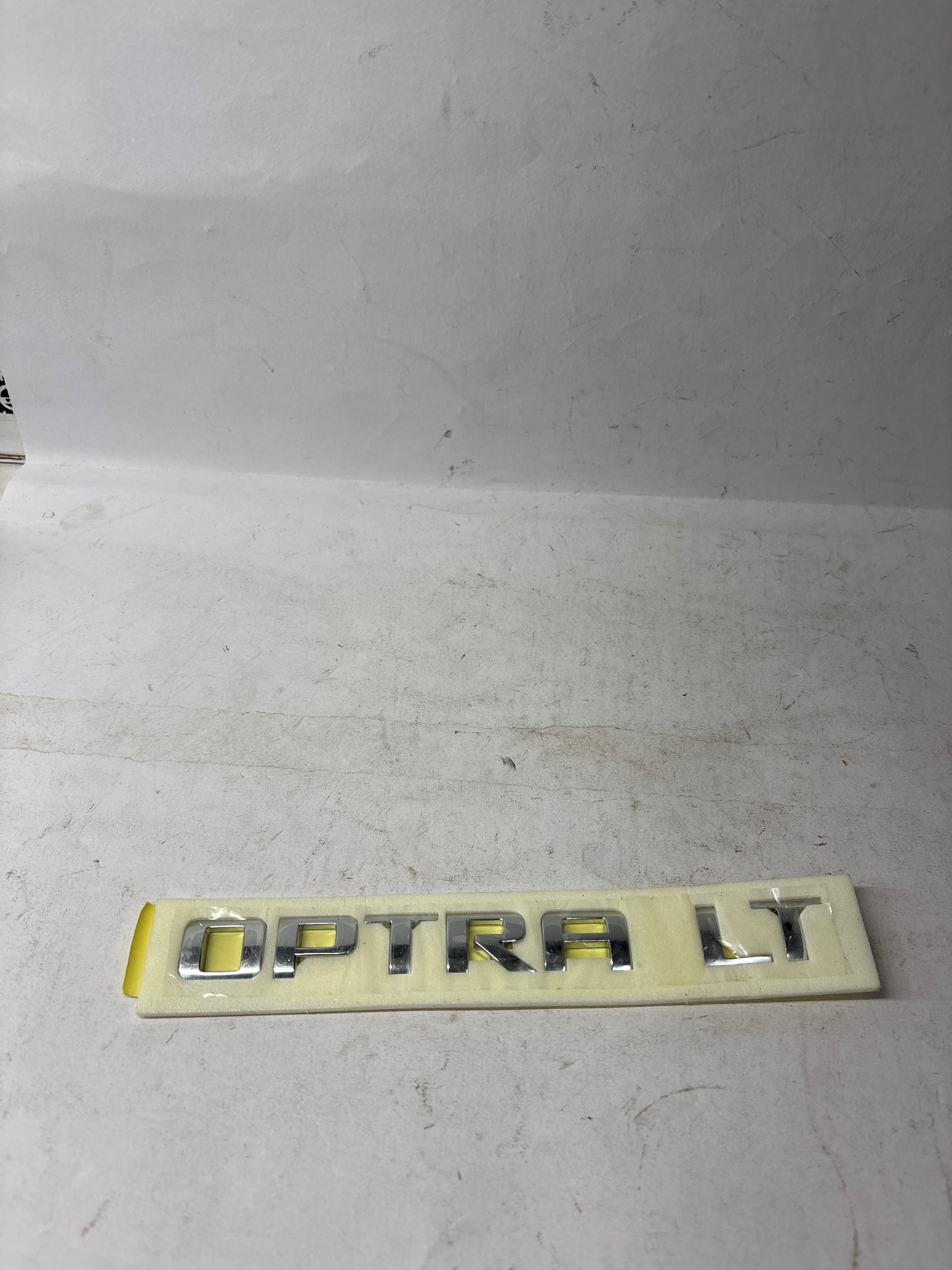 Lettering A Opel Optra LT petrol badge for General Motors vehicle, close-up shot showing the emblem details.