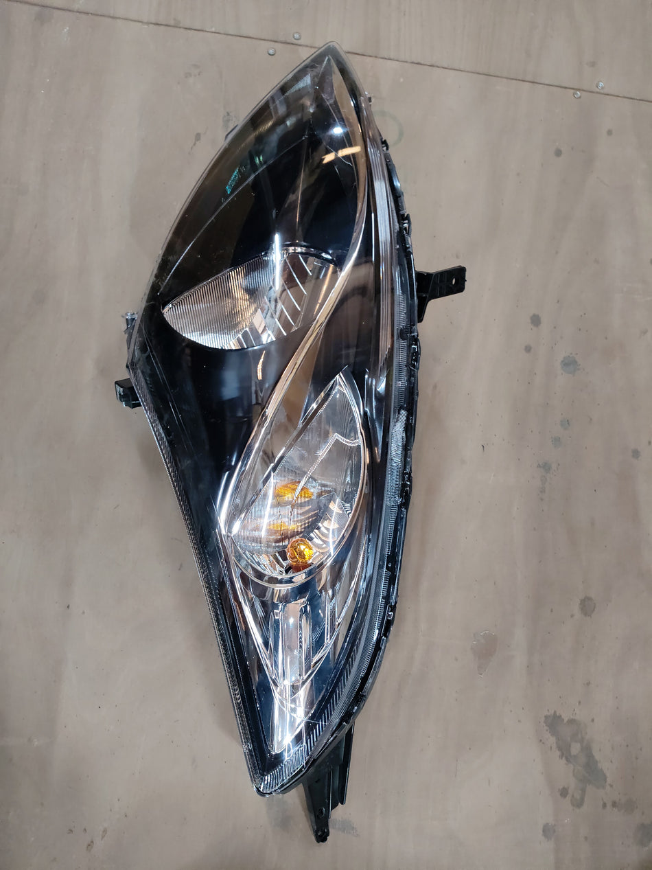 Maruti Suzuki head lamp assembly LH for vehicle, showing the front view of the headlight unit with clear lens and mounting brackets.