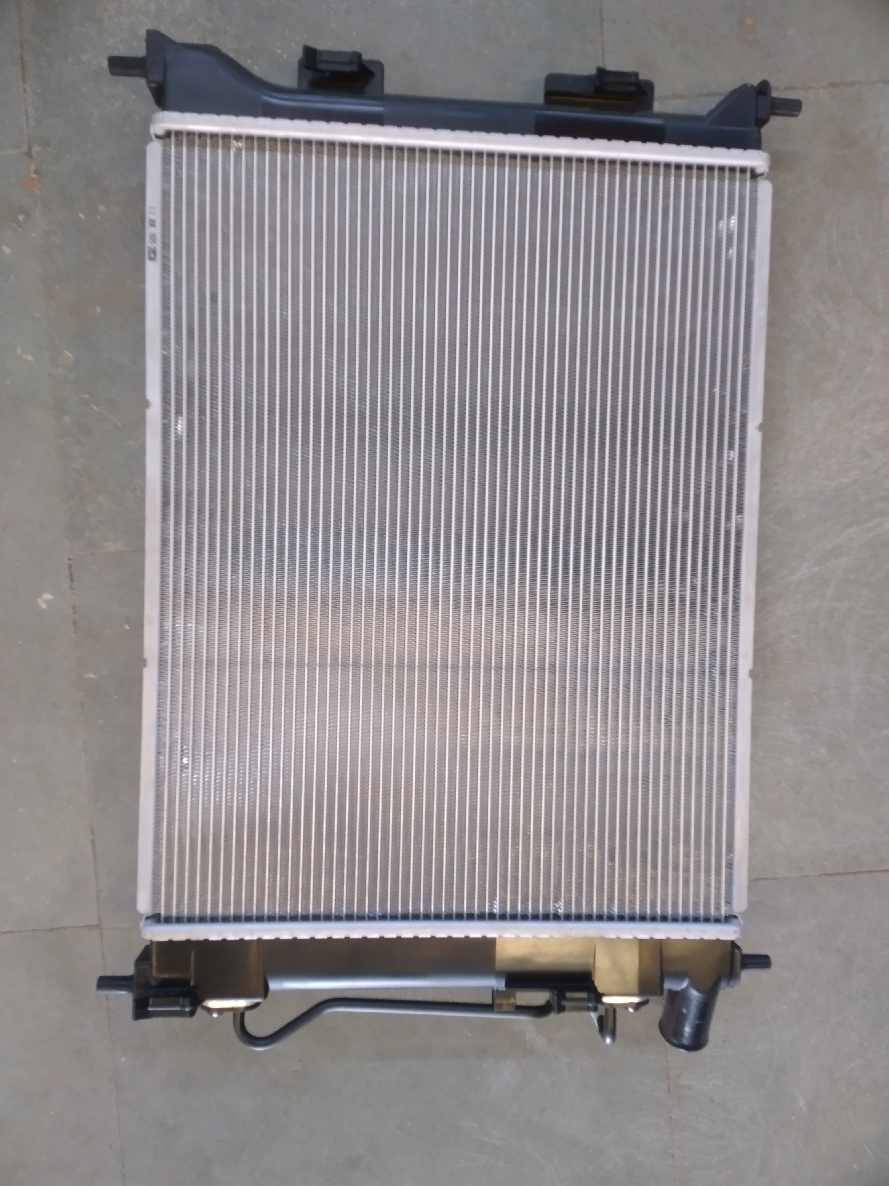 Hyundai 253100U050 radiator for Xcent petrol engine, new model, showcasing the front view with cooling fins and mounting points.